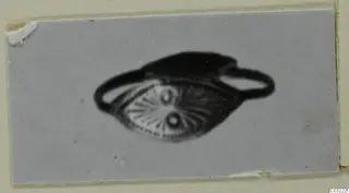 Ring with an oval bezel decorated with radiating lines and two dots, shown on a grey card mount