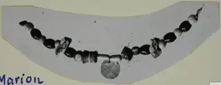 Necklace of dark and pale beads laid in a curve, with a flat disc pendant hanging from the centre