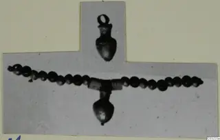 Two pendants on a strand of dark beads with a coiled-wire section at the centre, photographed on a mounted card