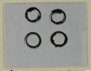 Four ring-shaped bronze personal adornments arranged in two rows on a pale grey ground