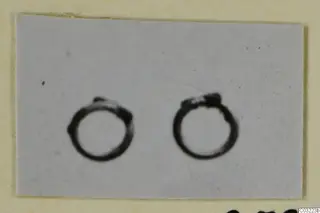 Two bronze personal adornments, plain ring-shaped objects, photographed side by side on a pale grey background