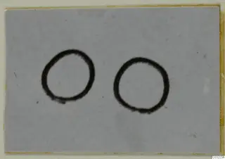 Two dark circular ring shapes on a pale grey card, set in a yellowed mount.