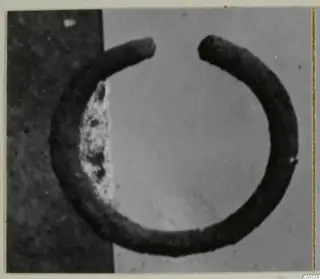 Open bracelet of dark metal, a thick band with two ends that do not meet, photographed on a grey ground