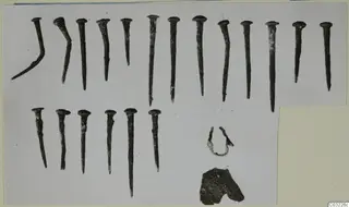 Corroded metal nails, a bent rod and small fragments laid out on a pale card