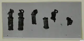 Six dark, corroded small metal objects, several with a loop at the top, shown on a pale grey ground.