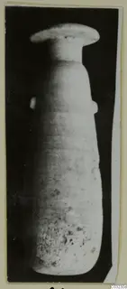 Tall stone vase with a flat disc-shaped rim and a small handle on each side, photographed upright against a dark background.