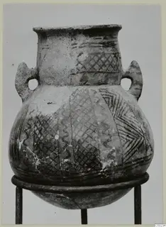 Two-handled White Painted pottery jar with crosshatched and zigzag bands, photographed on a metal stand.