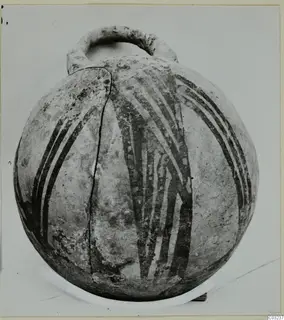 Round pottery vessel with a loop handle and dark painted bands, photographed against a light background.