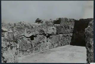 Stone wall of large squared blocks at the palace at Vouni, with a dark opening to the right.