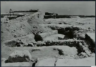 Excavated stone walls and blocks at the palace at Vouni, with a tripod standing at left.