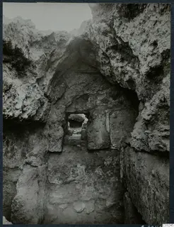 Narrow excavated cutting at Vouni palace, with rough rock walls and a stone-framed doorway opening onto a second passage