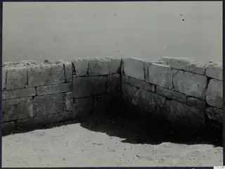 Corner of a stone wall of large rectangular blocks at the palace at Vouni, on a bare ground surface.