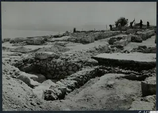 Excavated stone walls at the palace at Vouni, with workers near a small tree and the sea on the horizon