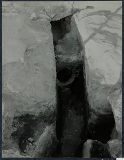Narrow excavated trench between large stone blocks at the palace at Vouni, with a round opening set into one side