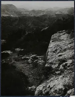 Hilly landscape seen from a rocky ridge at Vouni, with mountains on the horizon and scrub in the valley.