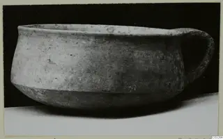 Plain white wheel-made pottery bowl with a single loop handle, from Milia