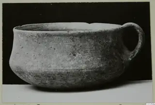 Plain pottery bowl with a single loop handle on the right, photographed against a black background.