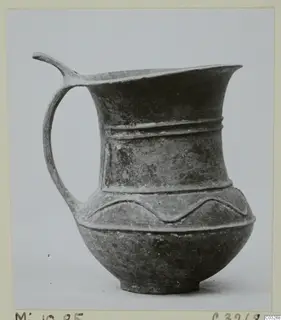 Pottery jug with a single handle, a pinched spout and raised horizontal bands, photographed on a plain background.