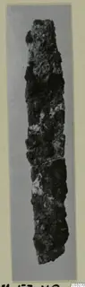 Corroded iron tool, long and narrow, shown upright on a grey background