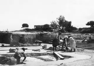 Workers laying a concrete floor over a cistern at Vouni, with stone steps and walls behind them.