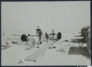 Workers repairing a channel and wall among stone blocks in Room 47 at Vouni, with a column drum standing nearby.