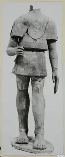 Headless terracotta statue of a standing figure in a short belted garment, on an oval base