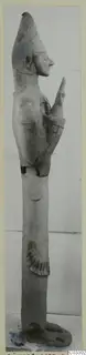Tall terracotta figure of a standing figure in profile facing right, one arm raised, with a conical head covering.