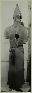 Terracotta statue of a standing figure with a tall conical headdress and comb-like incised marks on arms and skirt