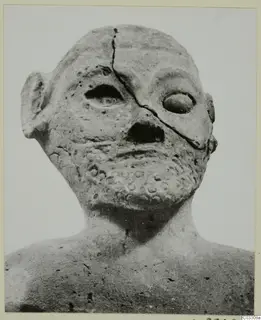 Terracotta head and upper body with a cracked face, a narrow slit eye, and a band of small round impressions on the chin