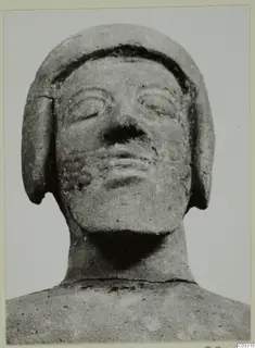 Frontal view of a terracotta statue head with incised eyes, nose and mouth, and a band over the hair.
