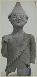 Terracotta figure with a tall pointed cap, large round eyes and a fringed diagonal garment across the chest