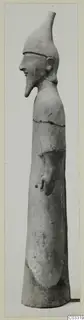 Side view of a pale clay standing figure with a tall conical headdress and pointed beard, from Ayia Irini
