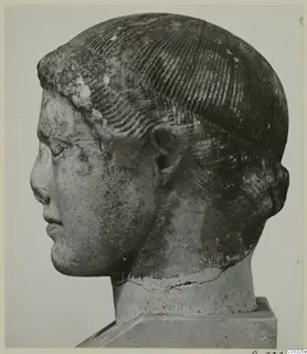 Carved stone head of a figure in profile facing left, with rows of incised hair, on a square base.