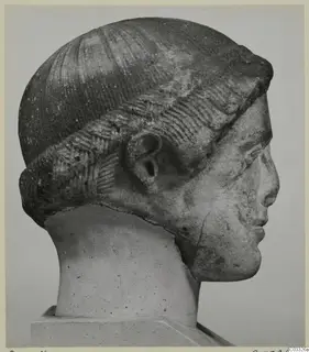 Carved head in profile facing right, with a tall rounded headdress of incised lines and a modelled ear.