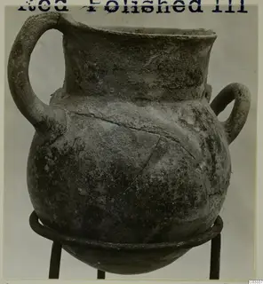 Red Polished III jug with a high loop handle and a second small handle, standing on a metal stand.