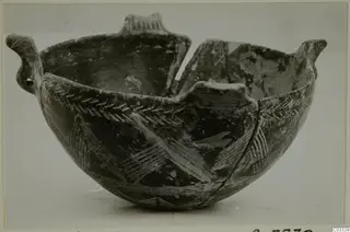 Broken pottery bowl with two upright handles and a dark body decorated with pale chevron and herringbone bands.