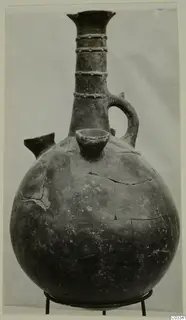 Red Polished II jug with a tall neck, ring-studded collar bands, a side spout and a loop handle, on a metal stand