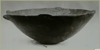 Dark pottery bowl with a wide, rounded body and small horizontal handles at the rim, shown in side view.