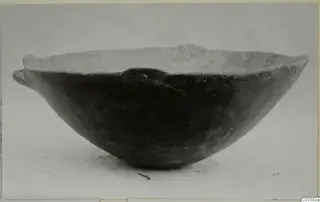 Dark polished bowl with two small handles on the rim, photographed in side view on a pale background