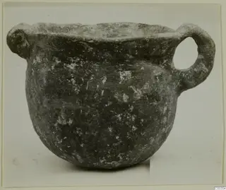 Round-bodied pottery vessel with a wide mouth and two handles, dark surface with pale flecks.