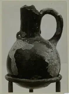 Red Polished III jug from Lapithos, with a single loop handle and broken rim, standing on a metal ring stand