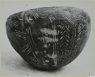 Dark polished bowl with incised herringbone and vertical line decoration, standing on a light surface.