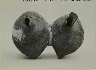 Pottery vessel of two rounded bodies joined at the middle, each with an open spout, standing on a plain background.
