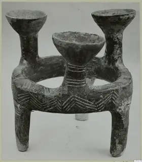 Dark pottery vessel with a ring-shaped body, three upright open cups and three legs, incised with chevron and band patterns