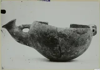 Pottery vessel in side view with a beak-like projection, a looped handle and two raised lugs at the top