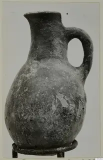 Red Polished III jug from Lapithos, with a single loop handle, standing on a metal ring stand