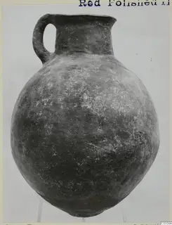 Red Polished II jug with a single loop handle, a short flaring neck and a rounded body, photographed on a clear stand