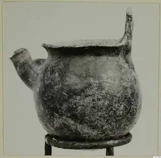 Pottery Red Polished II Bowl from Lapithos, shown on a metal ring stand, with a short spout and a tall handle