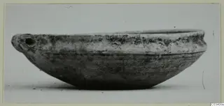 Plain white wheel-made pottery bowl with a small pierced handle, seen from the side.