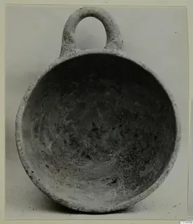 Pottery bowl with a single loop handle, plain white wheel-made, photographed from above showing its interior